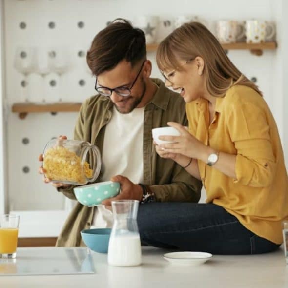 Man preparing breakfast for his partner with two bowls of cereal and milk