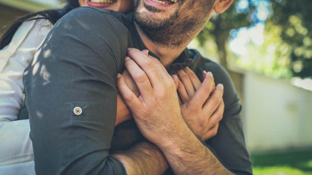 A woman’s arms wrapped around a smiling man outdoors.