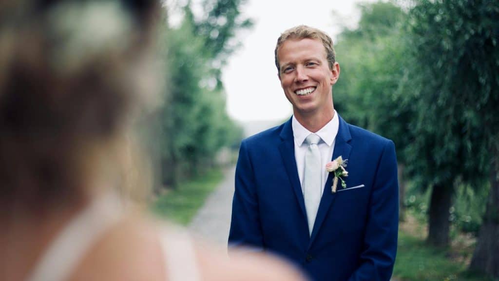 A smiling groom in a blue suit with a boutonniere.