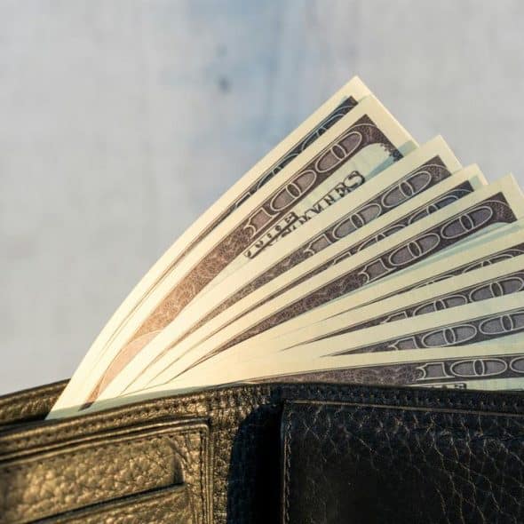 A black leather wallet holding a fanned stack of $100 bills.
