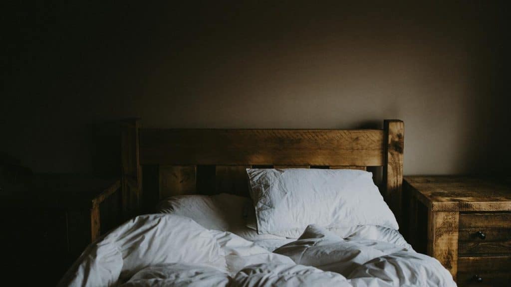 An unmade bed with white sheets and a wooden headboard.