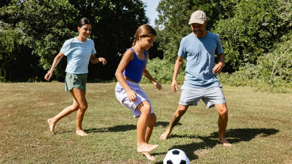 A family playing soccer barefoot on a grassy lawn.