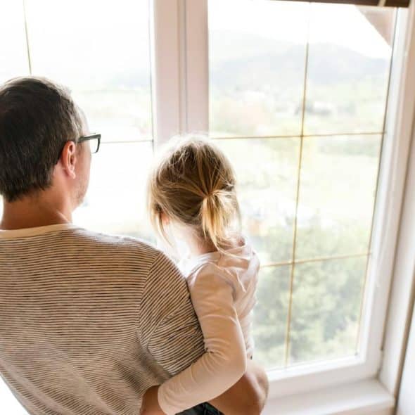 A man holding a child as they look out a window.