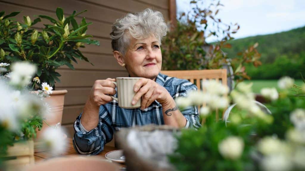 A mature woman with short grey hair sips from a mug on a patio.