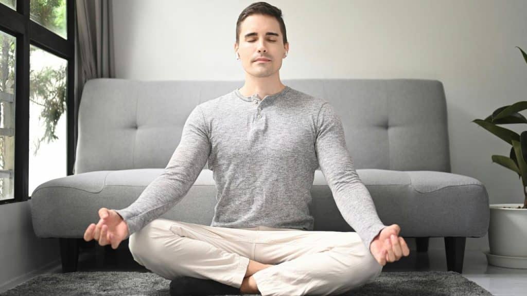 A man meditating cross-legged on the floor in front of a sofa.