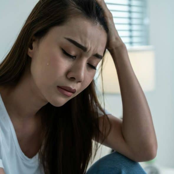 A distraught woman with long hair cries with her hand on her head.