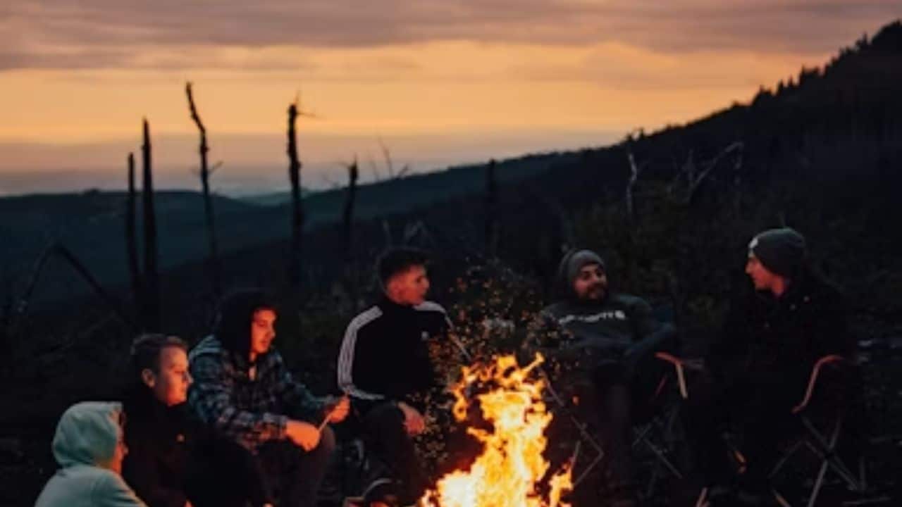 ALT Text: A man catching up with friends around a bonfire or dinner table.