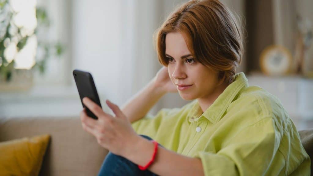 A young woman with short reddish-brown hair looks at her phone while relaxing.