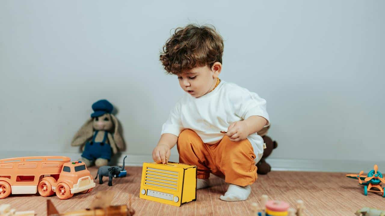 A toddler kneeling on the floor playing with a yellow toy radio.