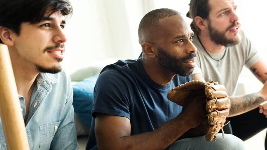 A trio of men watching a baseball game, one holding a glove.