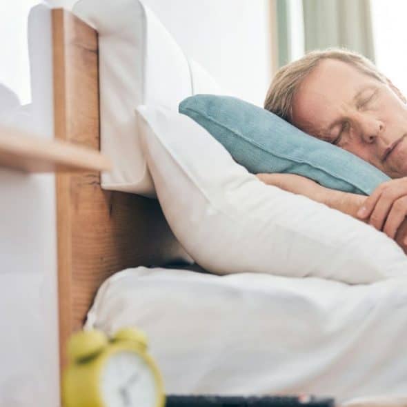 A man with closed eyes is sleeping soundly on his side in a bed.
