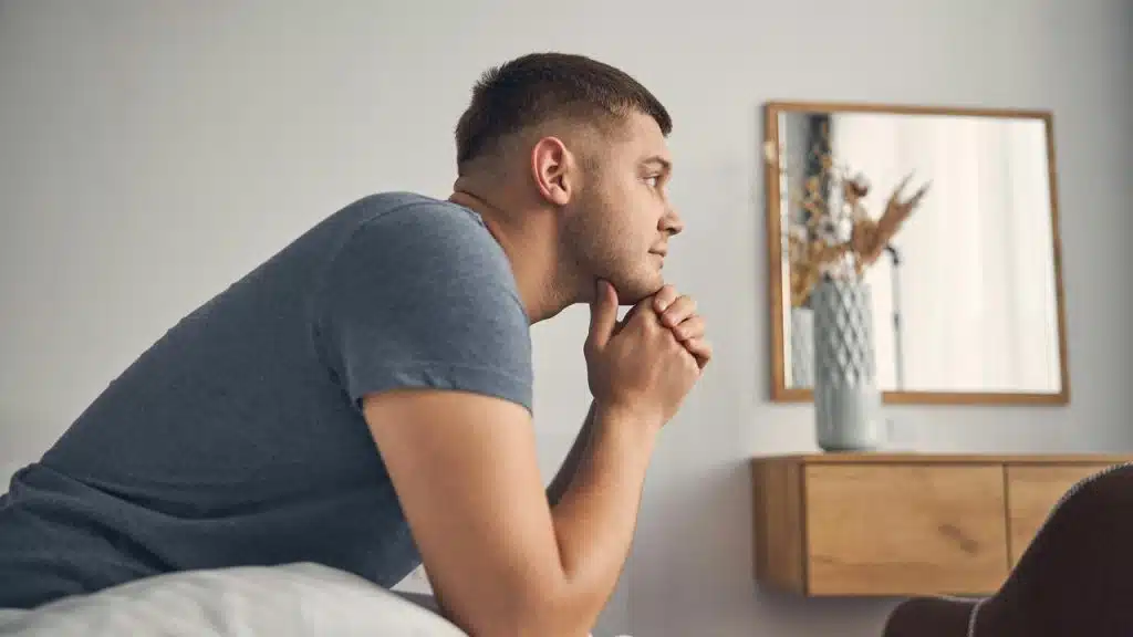 A man leaning on a bed with hands clasped under his chin.