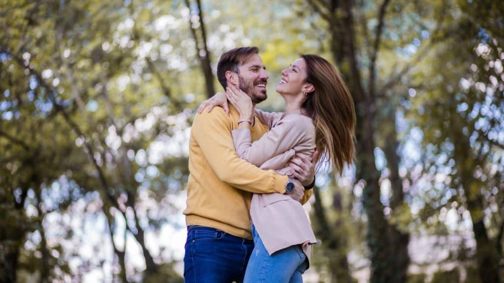 A couple joyfully embracing in a sunlit forest.