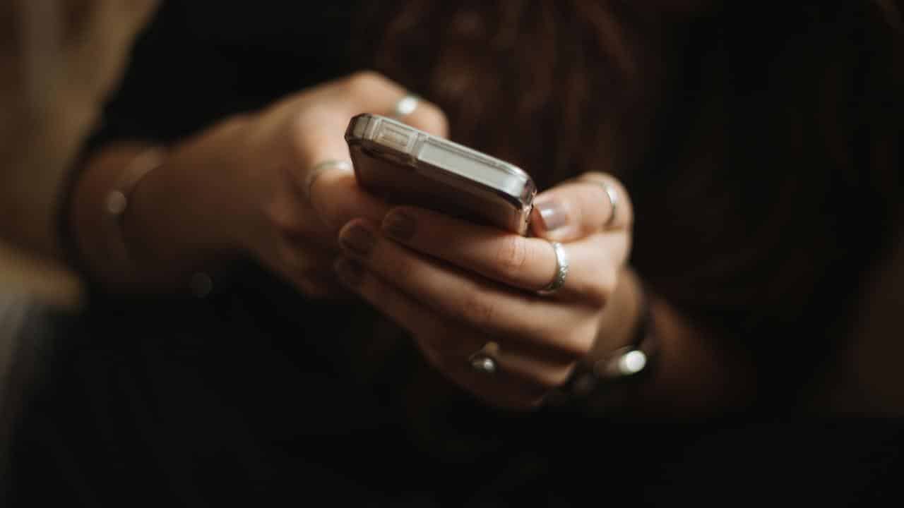 A close-up of hands wearing rings holding a smartphone.