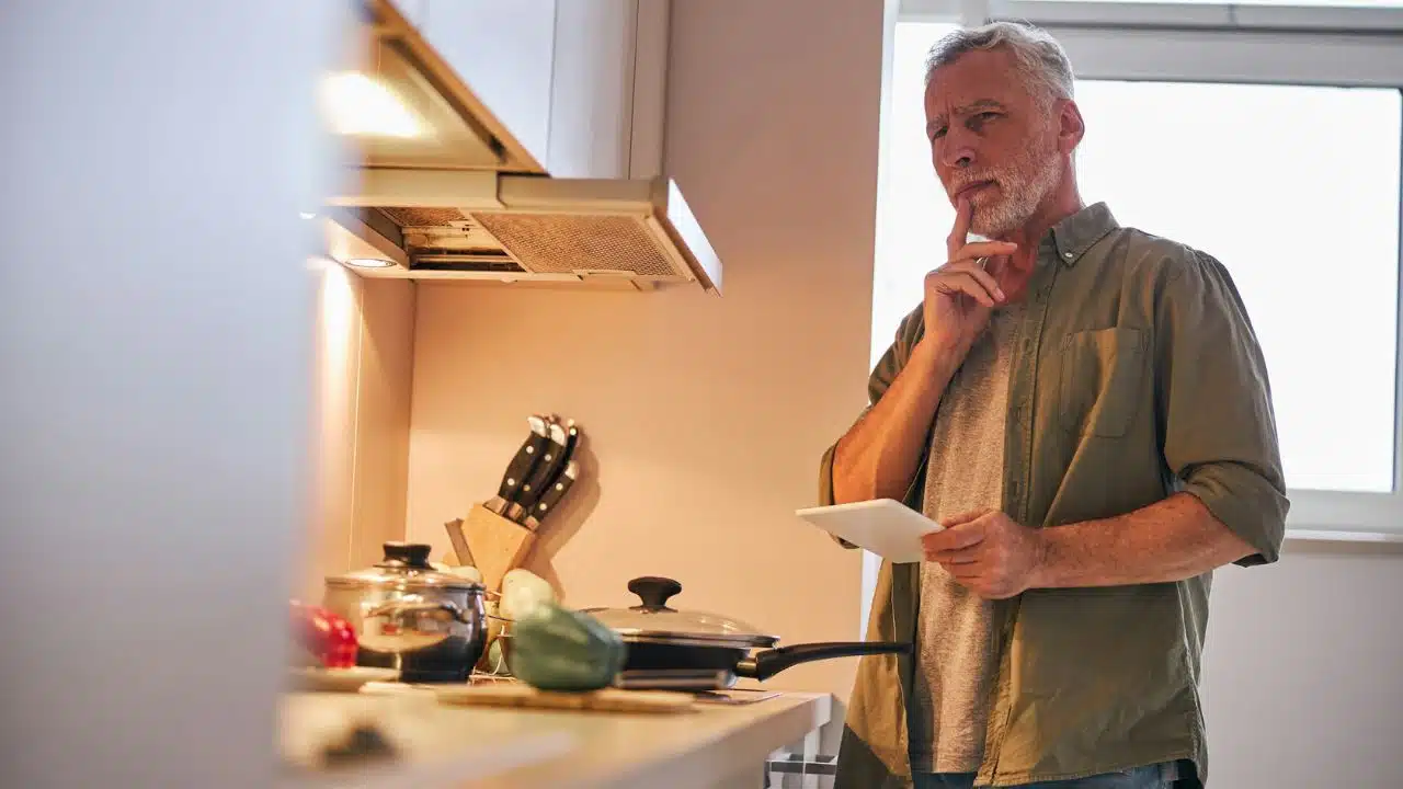 A contemplative man in a kitchen holds a tablet, pondering his thoughts