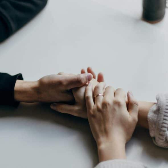 A close-up of two people gently holding hands across a table.
