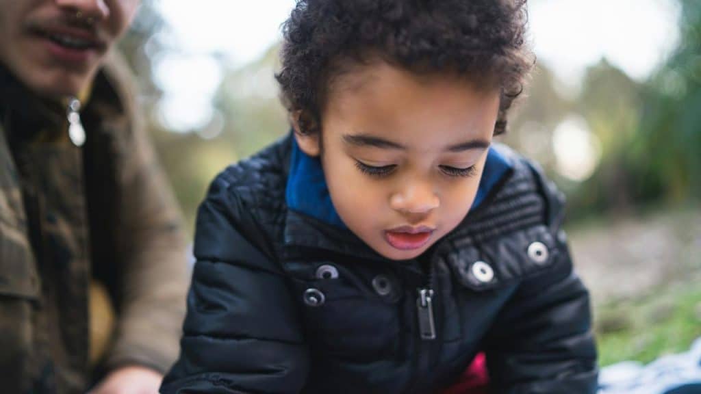 A young boy looking down thoughtfully outdoors.