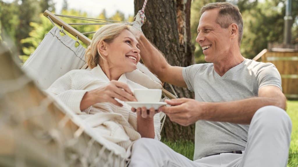 A joyful couple relaxes outdoors; a woman in a hammock sips coffee while a man smiles.