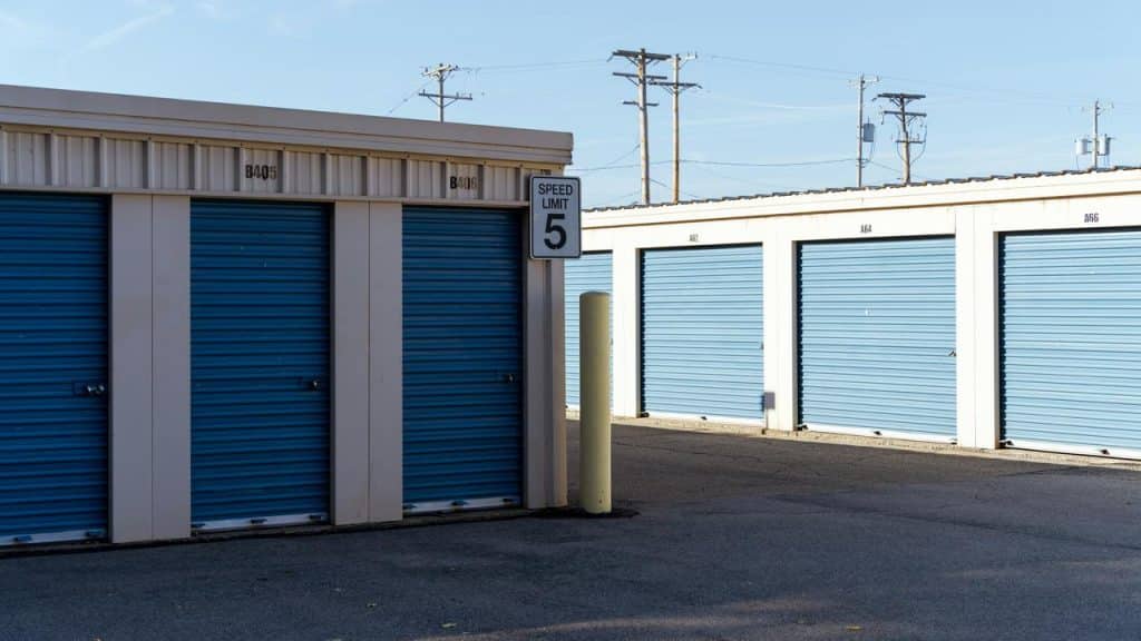 A row of storage units with blue roll-up doors and a “Speed Limit 5” sign.