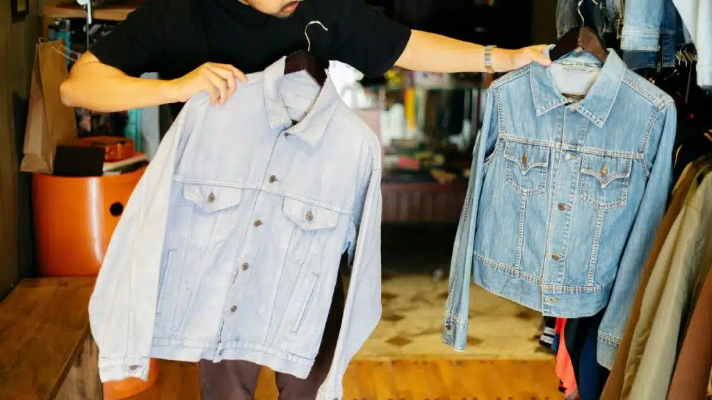 A person holding two denim jackets on hangers.