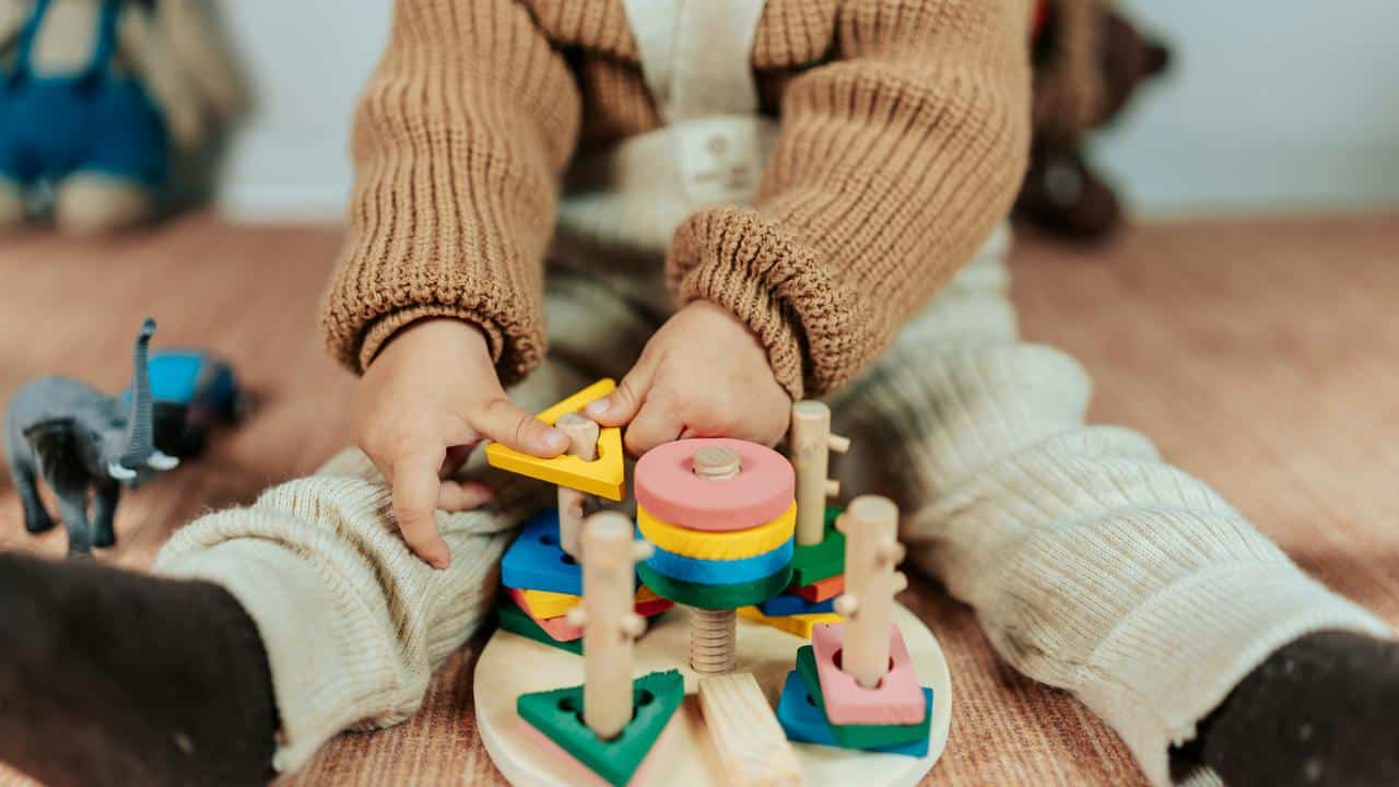 A toddler stacking colorful wooden shapes on a toy.