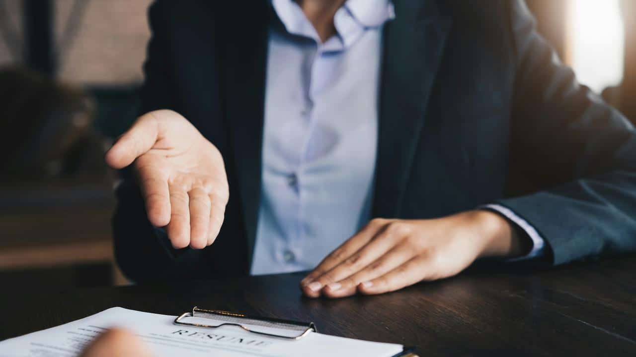 A suited person gesturing toward a resume on a table.