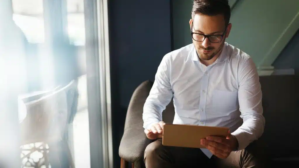 A man using a tablet while seated by a window.