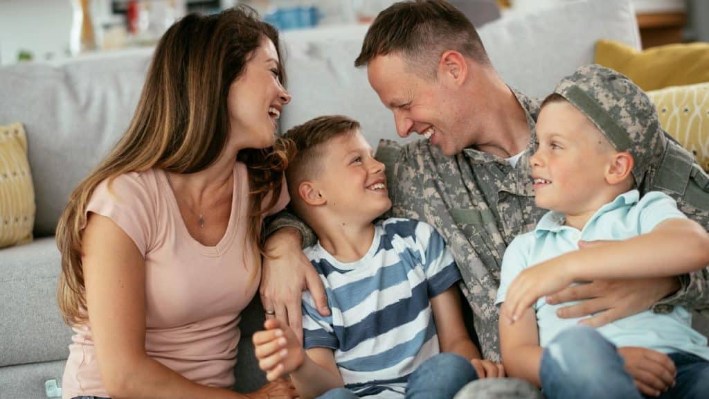 A soldier and his family smiling together on a couch.