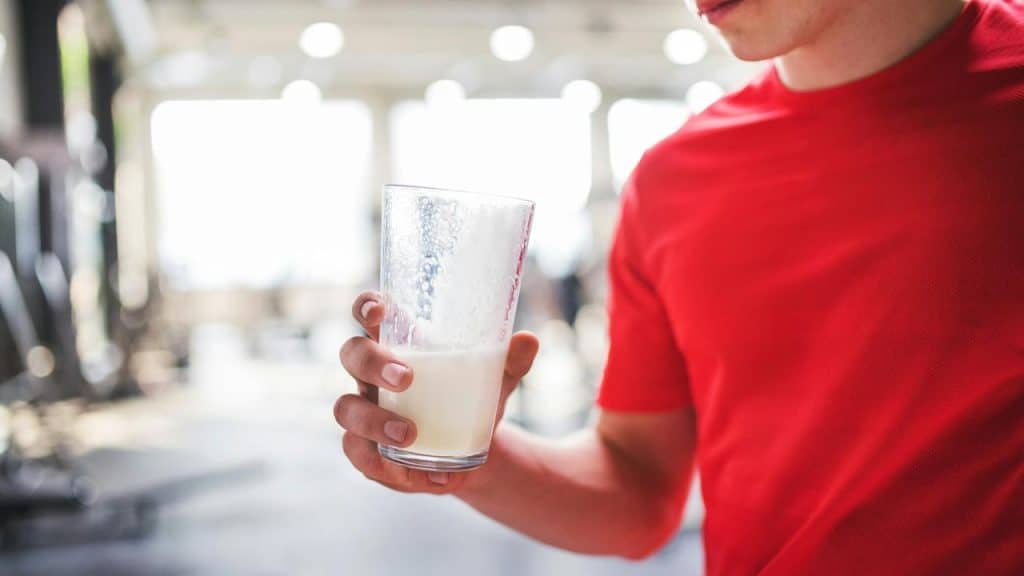 A person in a red shirt holding a half-full glass of milk in a gym setting.