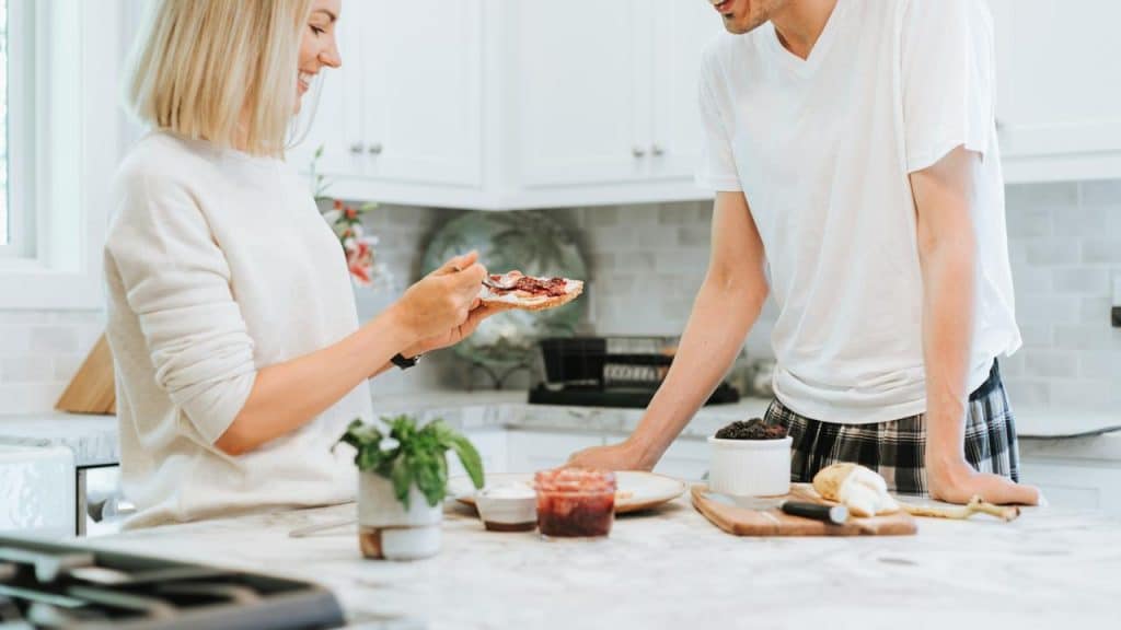 A woman spreading jam on toast as her partner watches at the kitchen island.