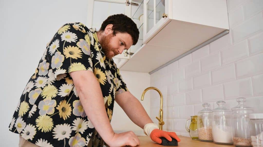 A man cleaning a kitchen countertop with a sponge.