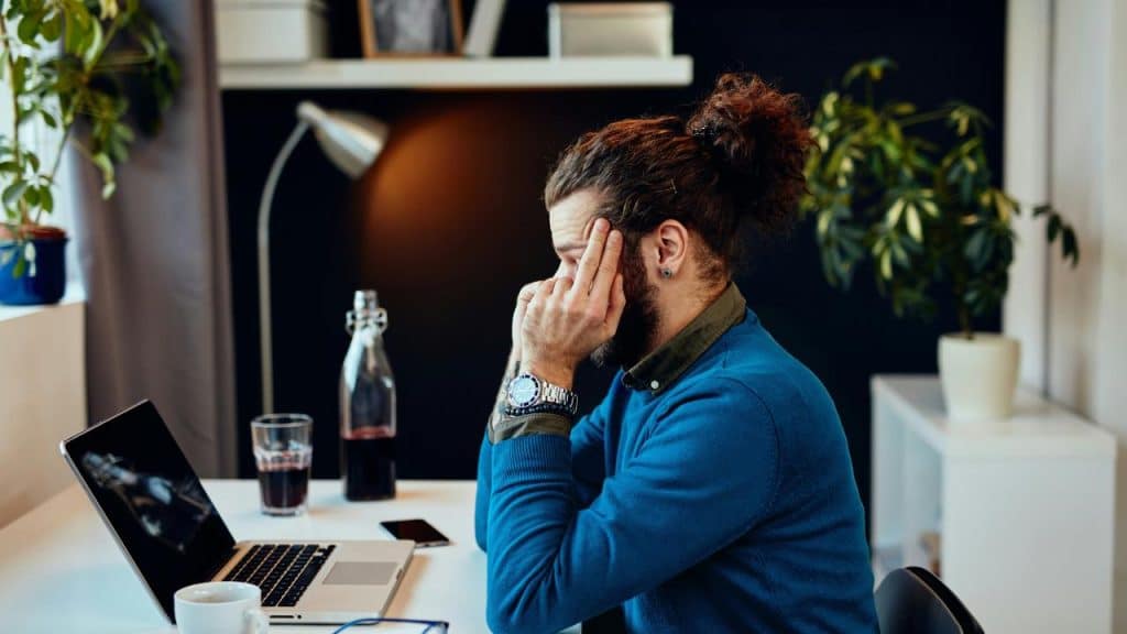 A frustrated man sitting at a desk holding his head.