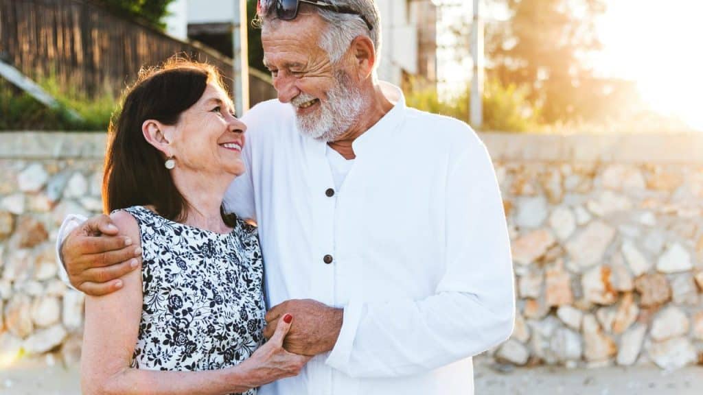 A smiling older couple embracing in warm sunlight.