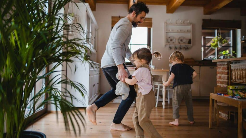 A father dancing with his daughter while his son walks by.