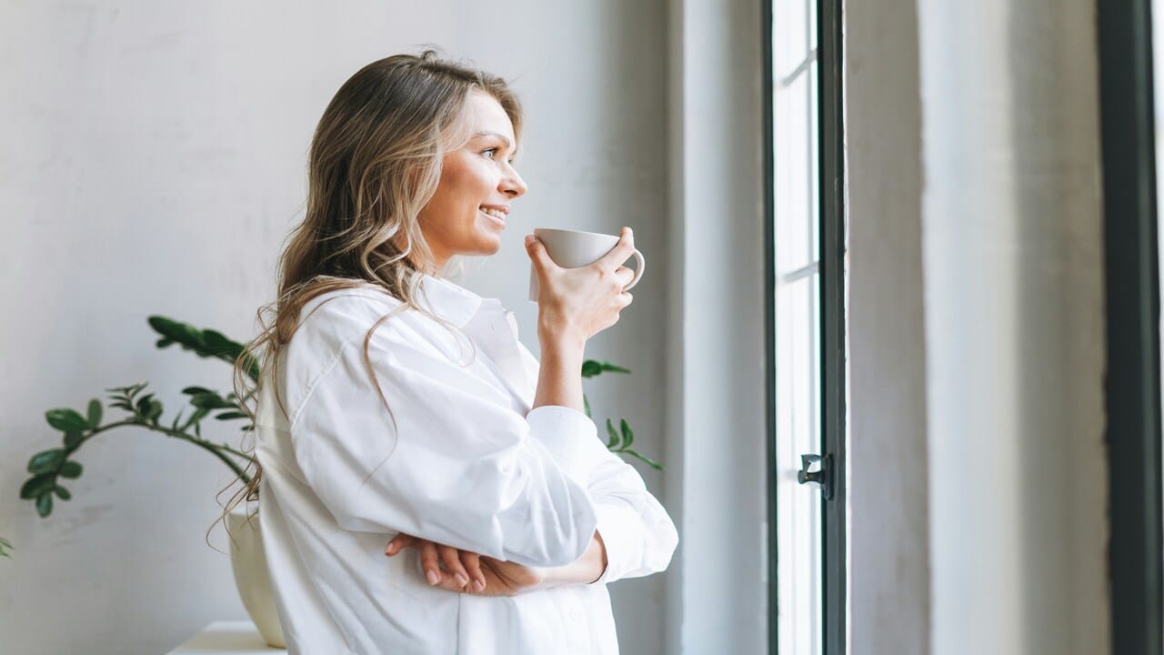 A woman looking out the window while having coffee.