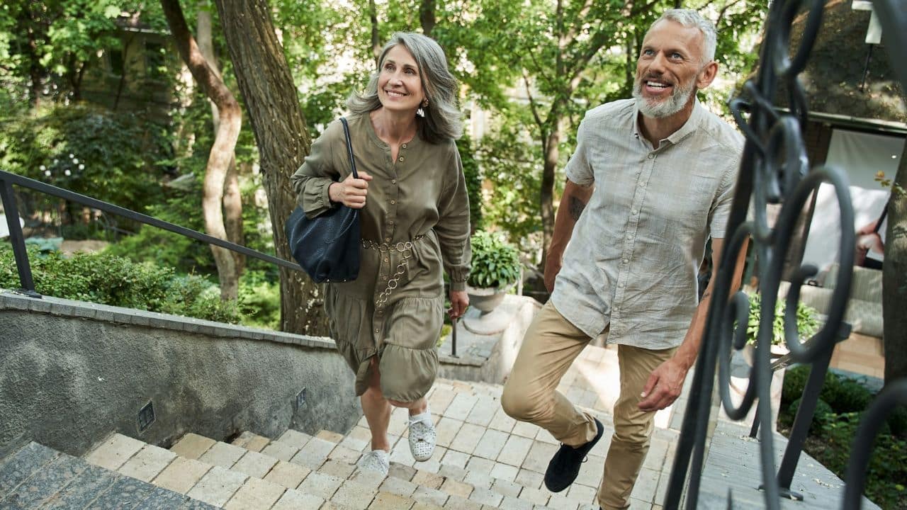 A happy, mature couple walks up outdoor stairs surrounded by greenery.
