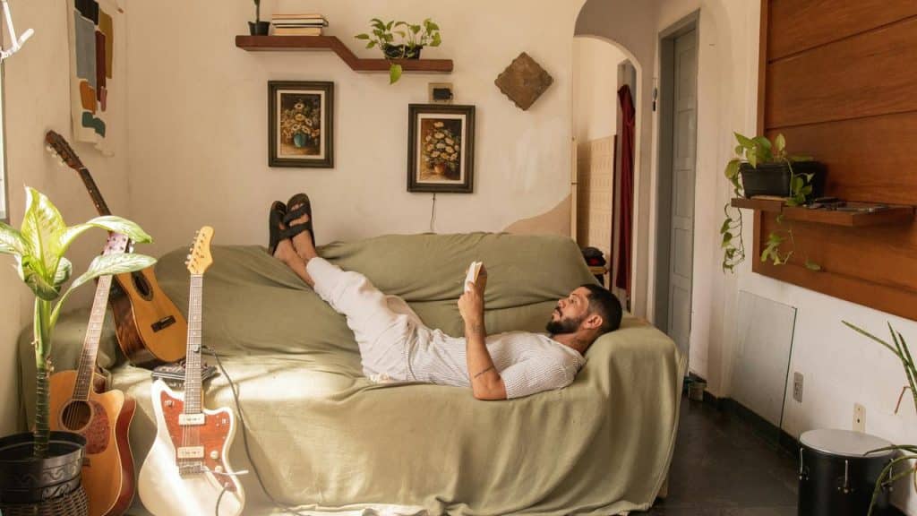 A man reading on a couch with guitars beside him.
