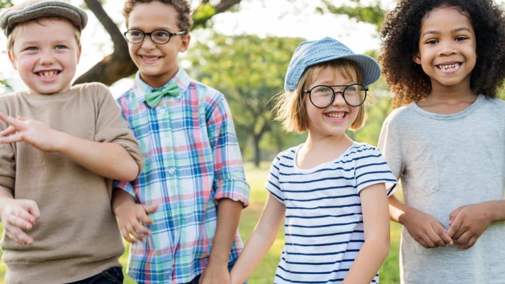 A group of four children holding hands and smiling outdoors.