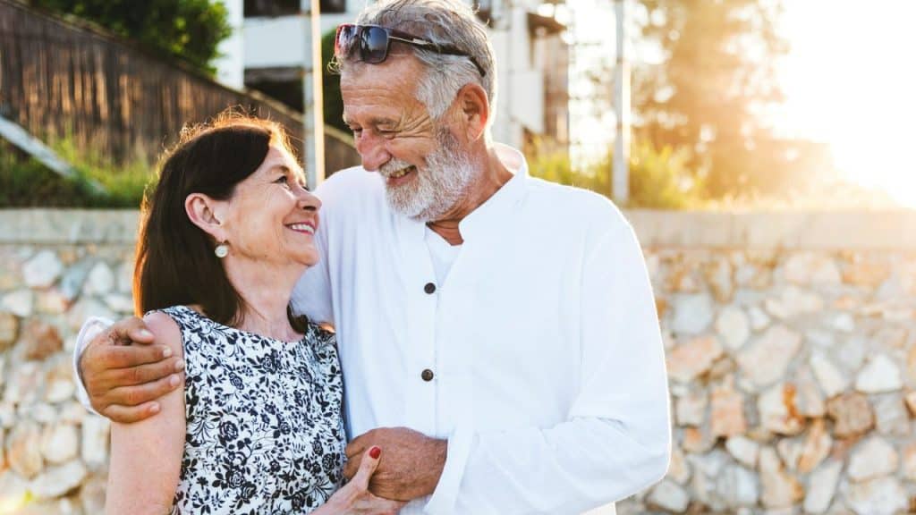 A joyful elderly couple, embracing outdoors, gazes affectionately at each other.