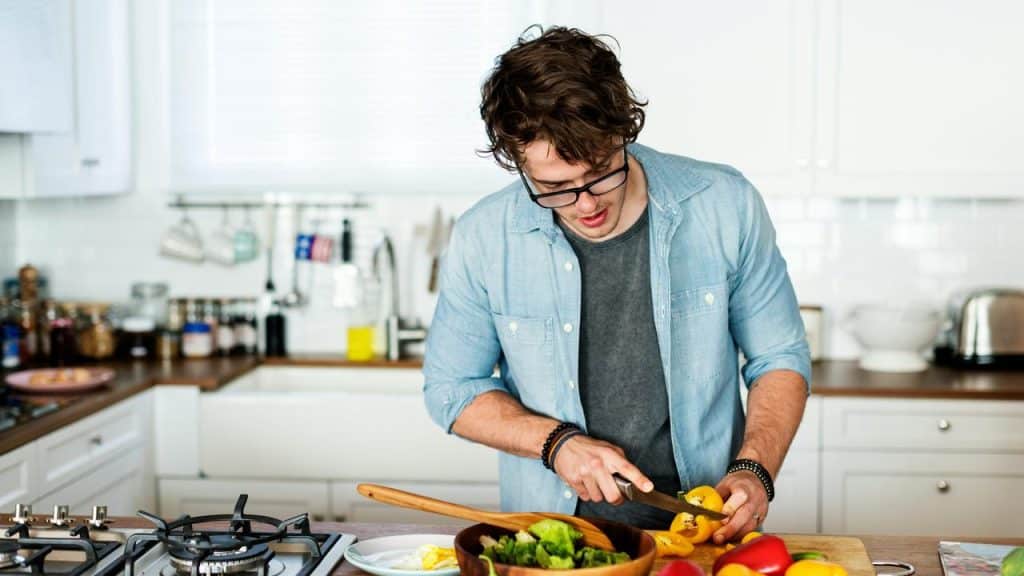 A man slicing a bell pepper over a salad bowl in a kitchen.