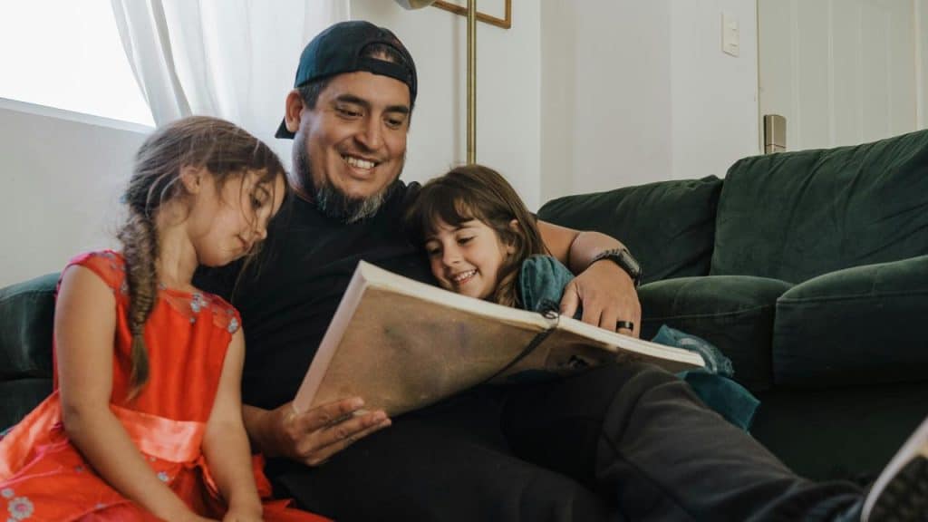 A man reading a book to two children on a couch.