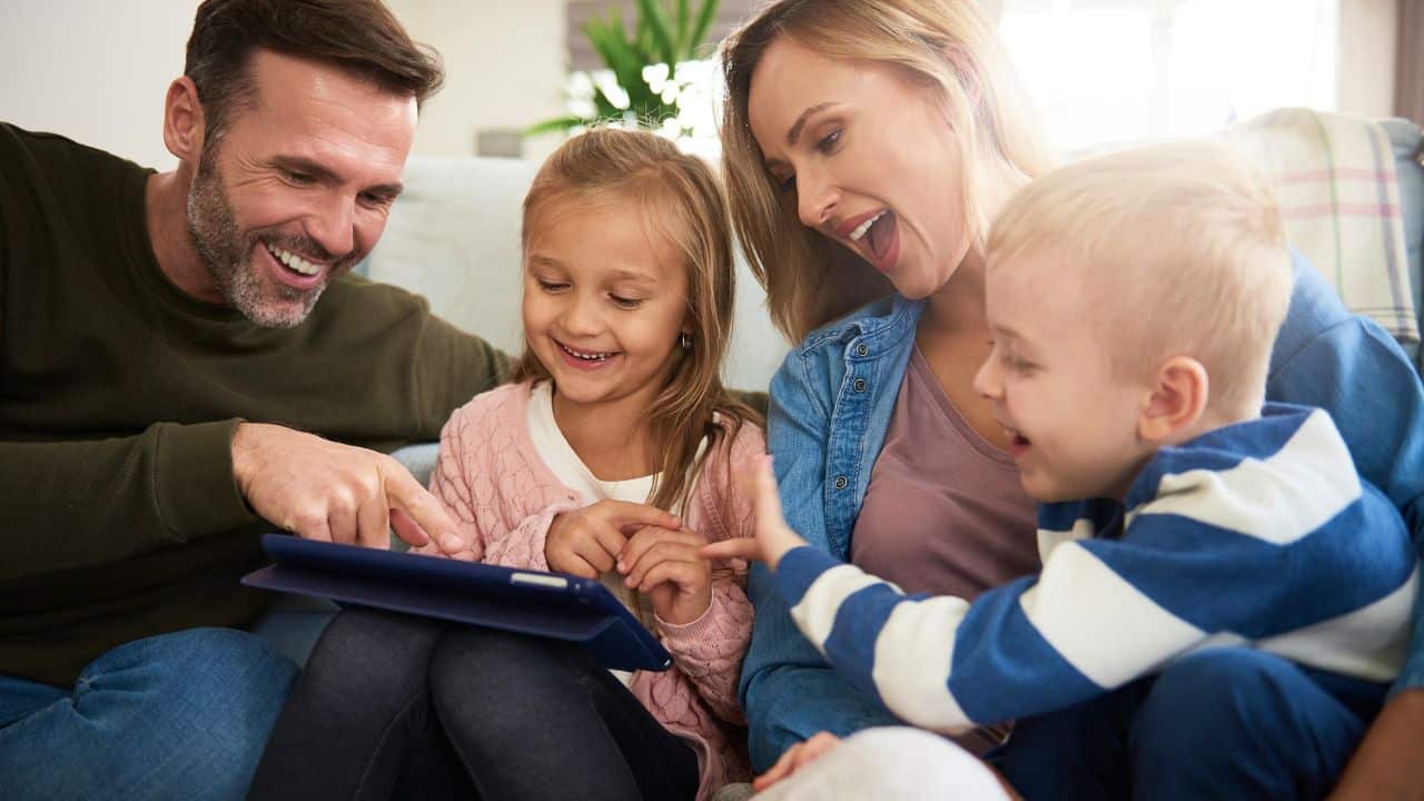 A happy family, mother, father, and two young children, are engaged with a tablet.
