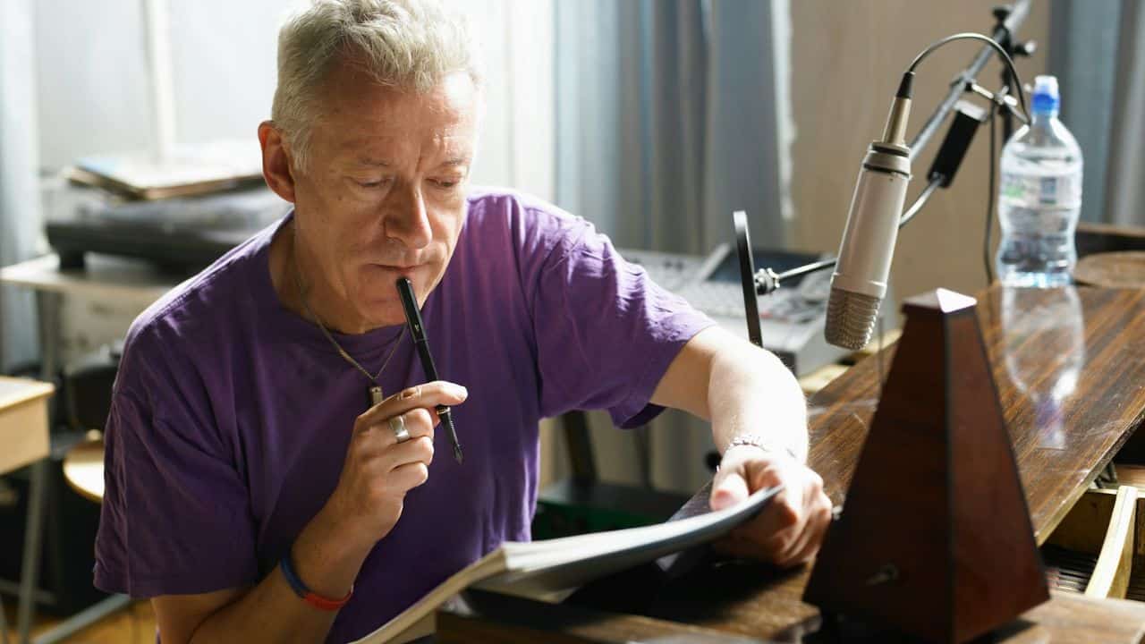 A thoughtful man in a purple shirt reads from a large book.