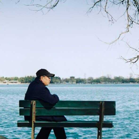An elderly man sitting on a bench by the water.