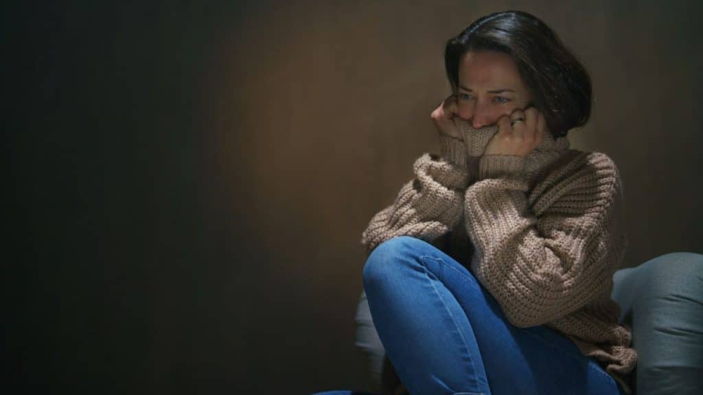 A woman in a chunky knit sweater and jeans pulls the sweater over her face, looking distressed.