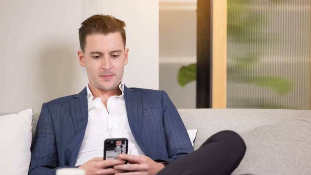 Man rethinking his daily “good morning” text while sitting on a sofa.