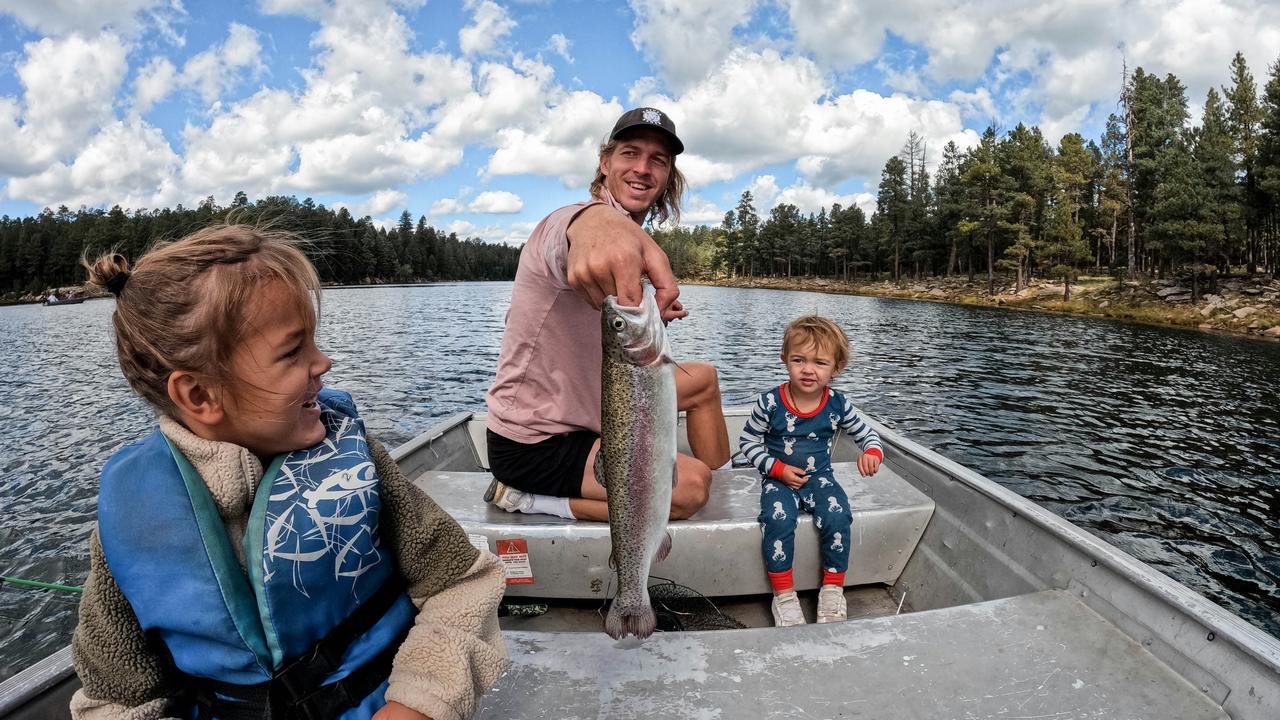 A man holding up a fish in a boat with two children on a lake.