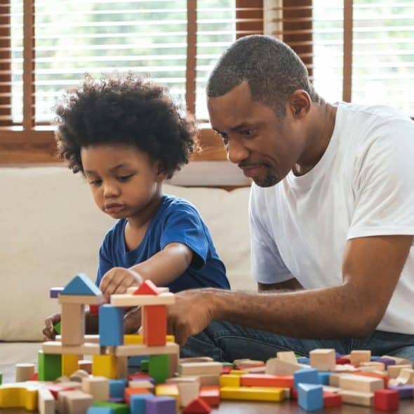 A man and child building a wooden block structure on a table.