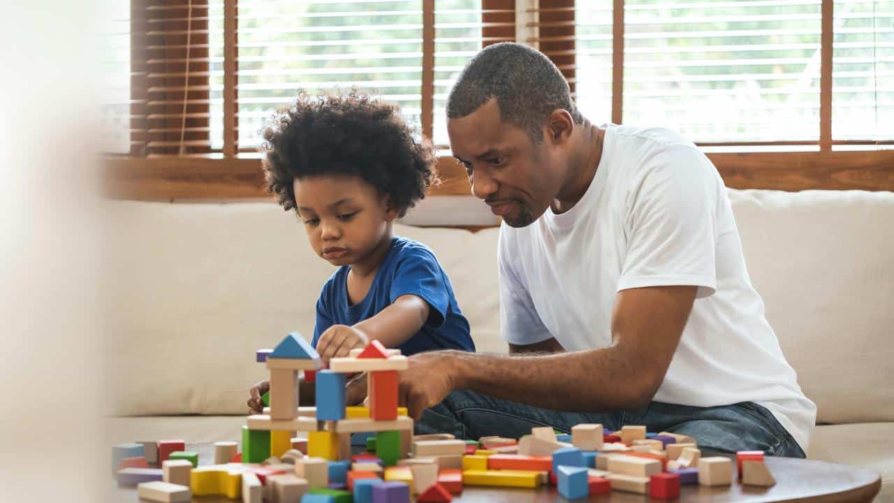 A man and child building a wooden block structure on a table.