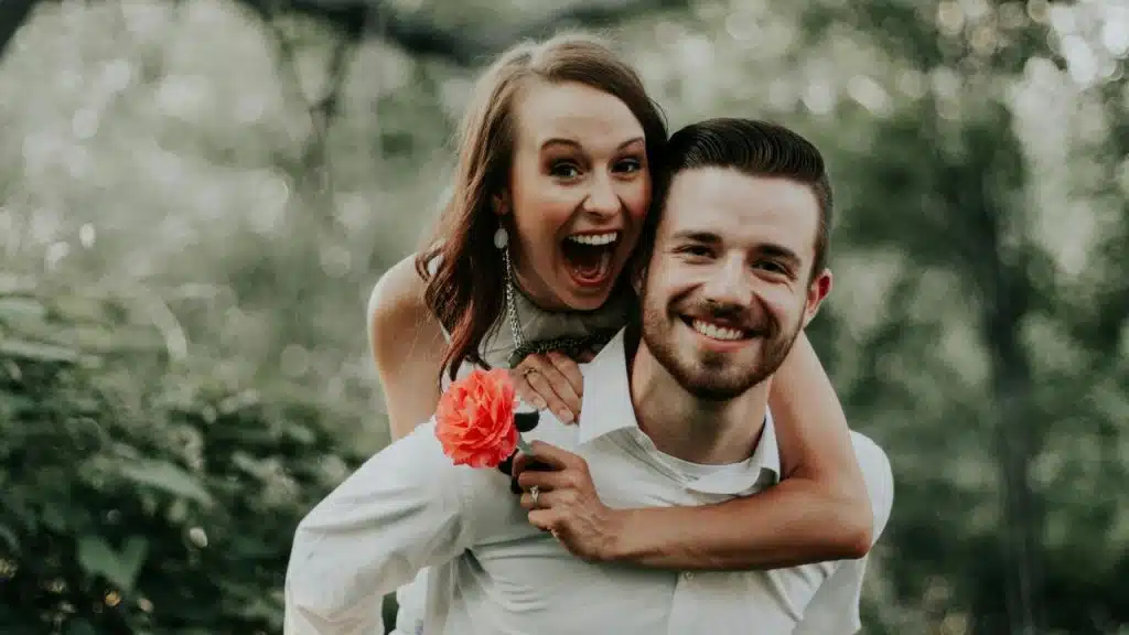 A man giving a piggyback ride to a smiling woman holding a flower.